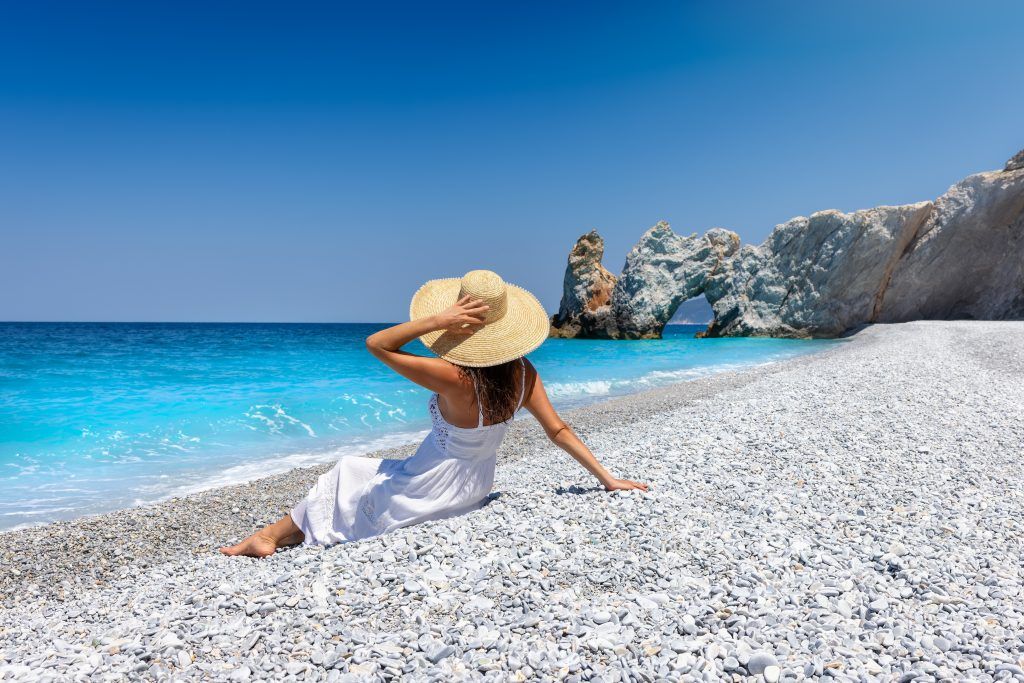Tourist enjoying Lalaria Beach Skiathos on white pebbles with arch view